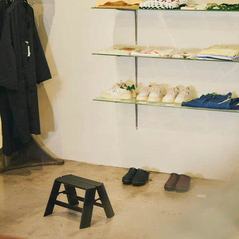 Ml10 1BK 1 Step Ladder Black With Folding Safety Bar in store setting, self-standing near shelves, grooved non-slip steps visible.