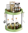 Two Tier 360 Degree Rotating Lazy Susan Spice Rack Organizer For Kitchen Countertop And Cabinet Pantry Storage Open Top With Guard Rails Extra Large 10 Inch Turntable Pro Grade Thickened PP Build For Easy Access And Spill Resistant in green, filled with bottles and jars, hanging utensils visible.