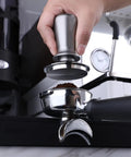 Hand using a silver tamper on an espresso portafilter, showing a Top-Tier Coffee Tamping Station With Built-In Espresso Knock Box And Portafilter Holder Keeps Your Bar Setup Crisp Fits 58mm Portafilters.