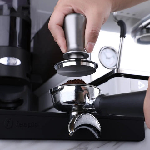 Hand using a silver tamper on an espresso portafilter, showing a Top-Tier Coffee Tamping Station With Built-In Espresso Knock Box And Portafilter Holder Keeps Your Bar Setup Crisp Fits 58mm Portafilters.