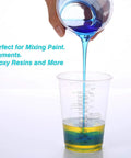 Hand pouring blue liquid into 100 Pack 8oz Graduated Clear Plastic Measuring Cups with Wooden Stirring Sticks for Mixing Paints Pigments Epoxy Resins