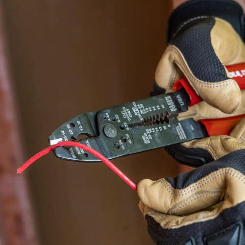 Electrician using American Made Multi Tool Wire Stripper Cutter And Crimper For 8-22 AWG on red wire in gloved hands.