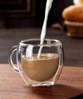 Cream being poured into a Double Wall Insulated Espresso Cups Set Of Two Borosilicate Glass Demitasse Mugs With Handle.