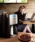 Coffee Maker Single Serve Espresso Machine With Blue Capsule Variety Pack For Office Kitchen And Home Use Quick Brews One Touch Operation Compact Desk Friendly Design Ideal For Breakrooms And Home Barista Fans next to a woman working in a cafe.