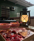 Bronze Outdoor LED Lantern With Vintage Flame Effect for Garden and Patio Decor next to table with raw meat trays.