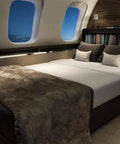 Luxury bed setup in a private jet cabin with plush bedding, pillows, and ambient lighting, featuring large windows.