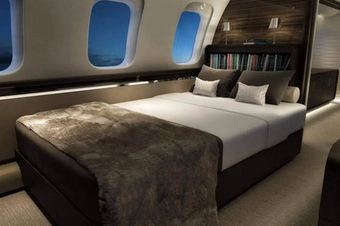 Luxury bed setup in a private jet cabin with plush bedding, pillows, and ambient lighting, featuring large windows.