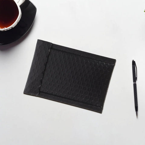 Black Padded Bubble Mailer Envelopes 12x18 and 4 Inch Thick Self Seal Plastic Shipping Bags on desk with pen