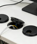 Premium Desktop Grommet Covers Slick Cable Organizers Hella Tough ABS Plastic Wire Routing Kit For Working From Home Office Setup No Mess Cord Management 5 Pack Black Two Point Five Inch Opening Sweet Fit Design on a desk.
