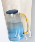 Liquid-filled glass jug with a blue lid and yellow handle, demonstrating stability on a tilted surface.