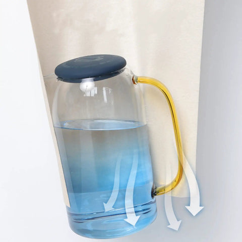 Liquid-filled glass jug with a blue lid and yellow handle, demonstrating stability on a tilted surface.