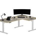Slick L Shaped Corner Standing Desk Electric Height Adjustment 72 By 48 Inches White Frame Bright Beech Top with monitor and laptop.