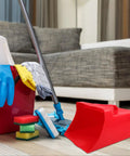 Red handheld dustpan and scoop shovel with 9.65x8.07 inch wide scoop, beside cleaning supplies on living room floor