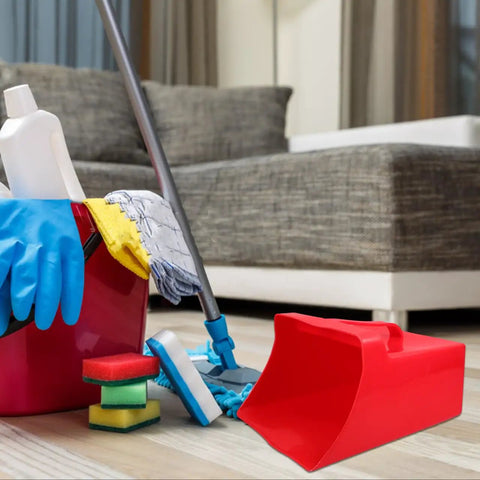 Red handheld dustpan and scoop shovel with 9.65x8.07 inch wide scoop, beside cleaning supplies on living room floor