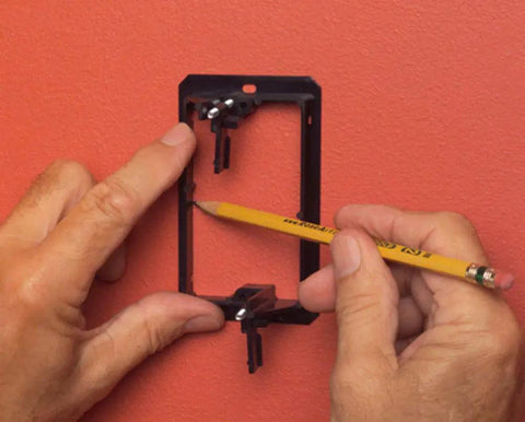1 Gang Low Voltage Mounting Bracket Pack Of 2 Black For Retrofit Telephone Coax And Network Wall Plates Fits Quarter Inch To One Inch Wall Thickness Horizontal Or Vertical Mount Flush Mounting being marked with pencil for installation on red wall.