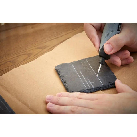 Person using 8 Piece Glass And Stone Accessory Micro Kit for carving lines on a dark slate tile, demonstrating engraving capability.