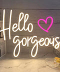 Hello Gorgeous Neon Sign For Girls Bedroom Wall Decor LED Light With Warm White Glow Perfect For Birthday Parties Weddings And Gifts 16.7x12.3 Inches Great Gift Idea displaying warm and pink glow on a marble desk.