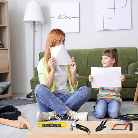 Mother and daughter playing with paper in living room, Kids Real Tools Set 30 Piece Builders Kit With Tool Box visible on the floor.