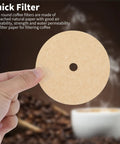 Hand holding Unbleached 3.75 Inch Percolator Coffee Filter Disc against blurred coffee beans and cup backdrop