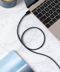 Braided black USB-A to USB-C charging cable connected to a gold laptop on a marble desk
