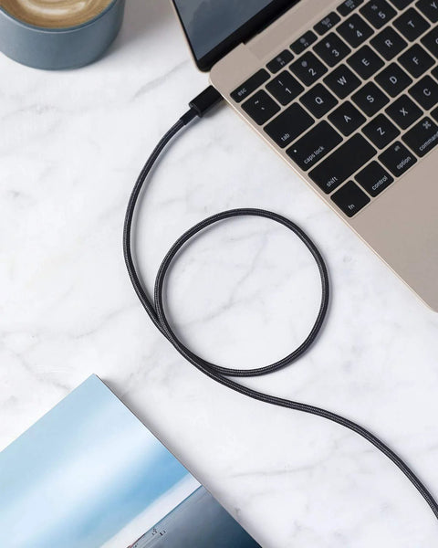 Braided black USB-A to USB-C charging cable connected to a gold laptop on a marble desk
