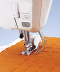 Quilting guide bar attached to sewing machine presser foot over orange quilt fabric