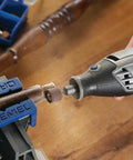 Front view of a Dremel rotary tool with grinding bit touching a metal rod secured in a blue vise.