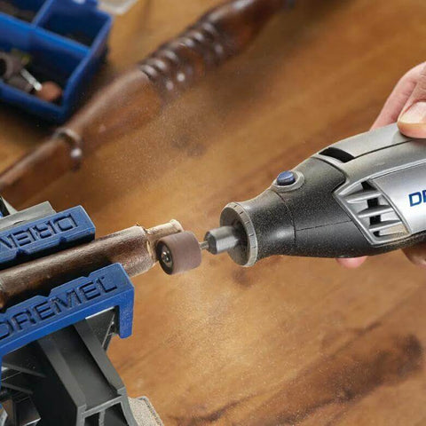 Front view of a Dremel rotary tool with grinding bit touching a metal rod secured in a blue vise.