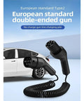 Heavy Duty Type 2 Electric Vehicle Charger Extension Cable With Smart Temp Sensor And Automatic Leakage Cutoff Spring Flex Coil Cord Up To Twenty Two Kilowatts, double-ended plug in front of a white car.