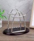 Pendulum Ball Desk Decor Set That Demonstrates Newton's Laws With Swinging Balls on a wooden desk with plants