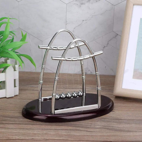 Pendulum Ball Desk Decor Set That Demonstrates Newton's Laws With Swinging Balls on a wooden desk with plants