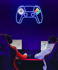 Gamepad Shaped LED Neon Sign for Gaming Room Decor illuminated on a wall above two gaming setups with chairs, creating a vibrant atmosphere.