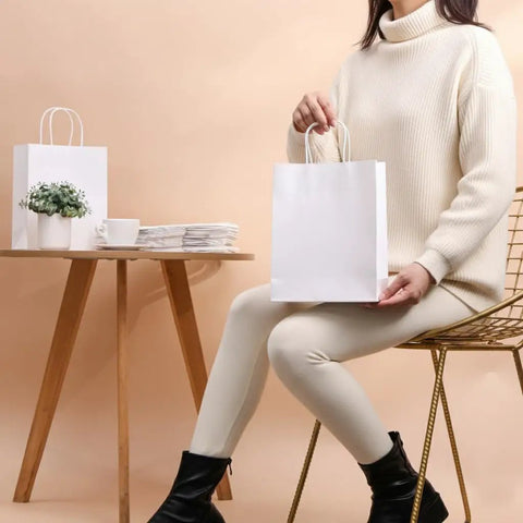 Woman holding White Kraft Paper Gift Bags With Handles Pack Of 25 Medium 8 By 4.5 By 10 Inches Tough Durable Recyclable Shopping Bags