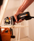 Hand using Compact Palm Saw With 3 Amp Motor And 3 3/8 Inch Blade on wood with clamp, showcasing ergonomic grip and lightweight design.