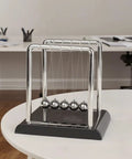 Cradle Balance Pendulum Balls Set With Black Base, kinetic fidget desk toy on a white table in an office environment