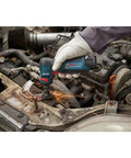 Compact 12 Volt Max Brushless Right Angle Die Grinder With Variable Speed Trigger in use, grinding metal in a car engine bay.