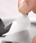 Close-up of hand peeling off an adhesive tab for 240 Pack Pvc Collar Stays For Mens Dress Shirts Invisible Anti Curl Adhesive Tabs.