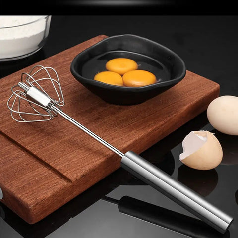 Stainless Steel Hand Push Rotary Whisk Blender Semi Automatic Kitchen Tool For Beating Eggs, Whipping Milk, Frothing Cream And Stirring, 12 Inch Durable Mixer Whisk Rod For Quick Pro Results next to a bowl with eggs and a cutting board.