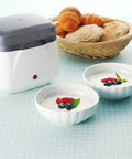 Dead Simple Compact Automatic Yogurt Maker With Food Grade Stainless Inner Pot And 360 Even Radiant Warmth For Smooth Homemade Dairy Culturing Right In Your Kitchen next to two bowls of yogurt topped with berries.