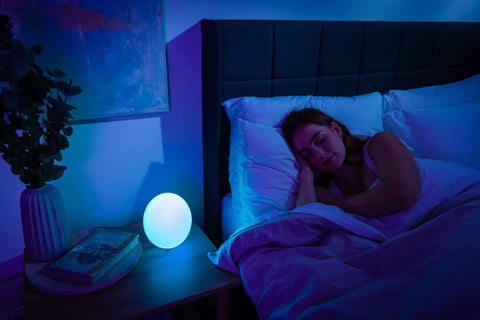 Bedroom scene with woman sleeping and Smart Led Entertainment Lamp And Night Light With 16 Million Colors on nightstand.