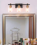 Three Light Industrial Bathroom Vanity Sconce With Black Gold Finish over a mirror, featuring clear glass shades.