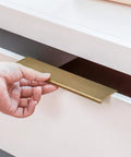 Hand installing Champagne Bronze Edge Finger Pull Cabinet Handle Six And One Quarter Inch Center to Center 160mm on white drawer