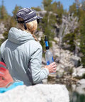 Person by lake holding Palm Sized Mini Water Filtration System SP128 Blue For Hiking Camping Travel And Emergency Prep Ultra Lightweight