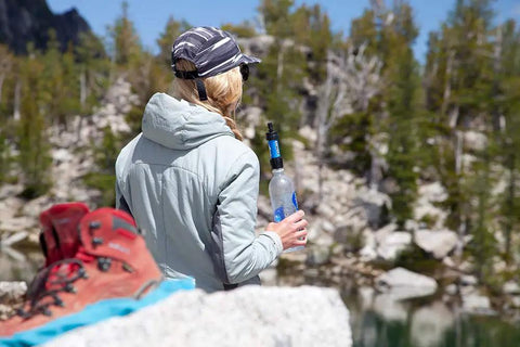 Person by lake holding Palm Sized Mini Water Filtration System SP128 Blue For Hiking Camping Travel And Emergency Prep Ultra Lightweight