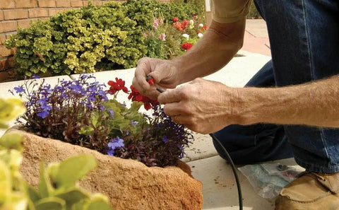 Man using Drip Irrigation Repair And Expansion Kit With 102 Universal Parts to fix garden drip system tubing and connectors