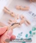 Top Shelf 100 Piece Mini Wooden Clothespins With Handy Storage Bag Dead Serious Grip Birch Hardwood Clips shown in hand with easy pinch feature.