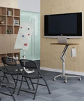 Game Changer Height Adjustable Standing Desk With Silky Gas Lift And Ultra Quiet Lockable Rubber Wheels next to a TV in a modern office.