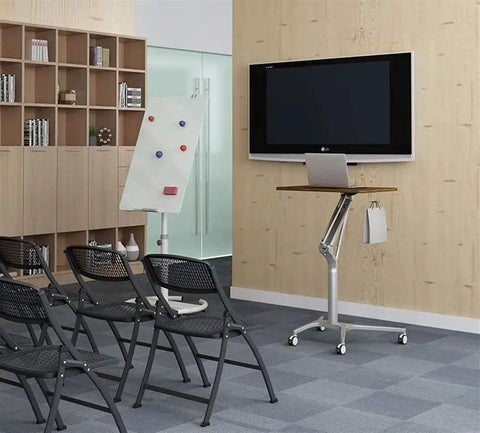 Game Changer Height Adjustable Standing Desk With Silky Gas Lift And Ultra Quiet Lockable Rubber Wheels next to a TV in a modern office.