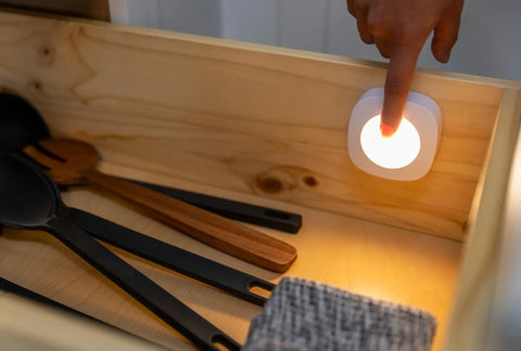 Tap On Off LED Light Stick-On Battery Powered Wireless Portable Light for cabinets, illuminating utensils in a drawer.