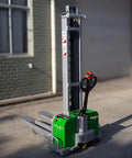 All Electric Dump Forklift Pallet Stacker With Portable Lifting Truck And Fixed Cross Leg Design Built Tough For The Daily Grind While Smashing Through Heavy Loads With Zero Sweat Featuring A Massive 2204 Pound Capacity And Six Foot Lift. Green electric pallet stacker with gray mast and compact base.